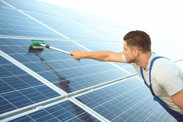 Young worker washing solar panels after installation outdoors