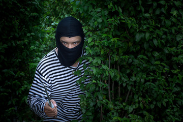 A terrorist or robber is standing behind the bush with knife and  looking at camera/Selective focus/criminal concept