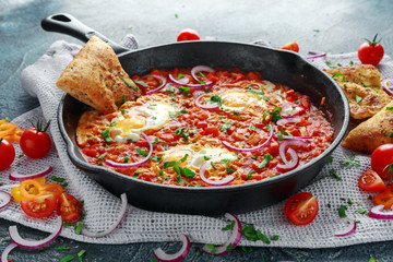 Tasty Breakfast Shakshuka in a Iron Pan. Fried eggs with tomatoes, red, yellow peppers, onion, parsley, Pita bread and herbs. Healthy Food