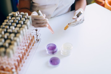 Obraz premium Female scientist holding white transparent tube with orange solution inside.