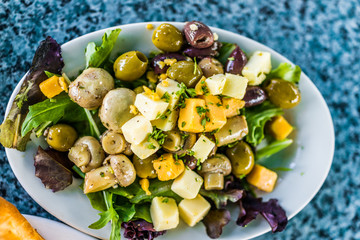 Macro closeup of salad on plate in restaurant with mushrooms, cheese squares, olives and greens