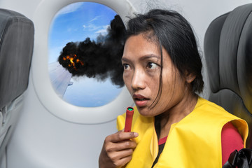 Scared woman on the plane listening to instructions for survival. The passenger on the plane dressed in life jacket. The accident aircraft burning wing.