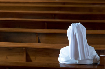 The nun sits in the church and prays to God. A nun in traditional white robes meditates in a...