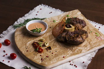 The large roasted piece of meat on the bone with sauce and spices on wooden board