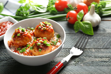 Delicious meatballs with rice and sauce in bowl on table