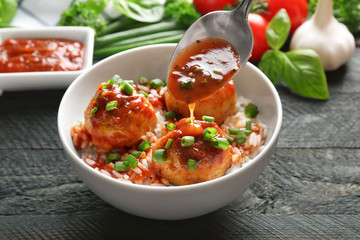 Pouring sauce onto delicious meatballs and rice in bowl on table