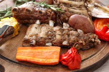 Wooden board with grilled ribs and vegetables, closeup