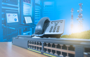 IP telephone on networking switch with blurred server rack cabinet data center room and telecommunication tower