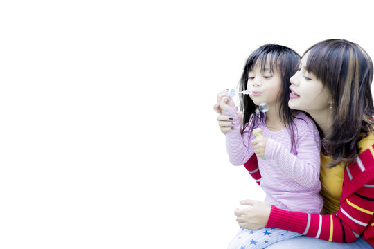 Mother with daughter blowing soap bubbles on studio