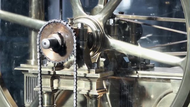 An old brass industrial beam engine wheel spinning with a chain.