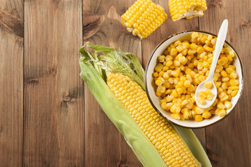 Corn cob and kernels in bowl on wooden background