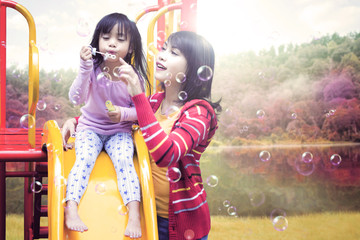 Child and mother playing soap bubble on slide