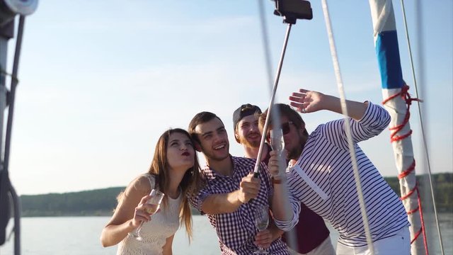 Happy friends enjoying party on the yacht. They having drinks and making mobile selfie to share it in social media