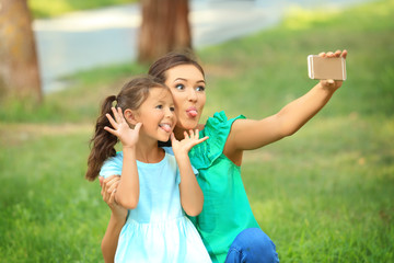 Cute little girl and mother taking selfie in park on sunny day