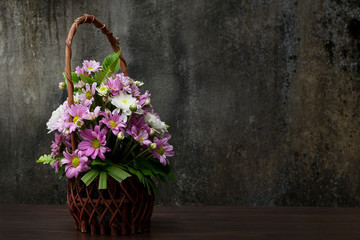 White and violet chrysanthemums or mums flowers in wooden basket brown on the table beside the dark wall. Selective focus and Still life style as space for text.