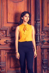 Modern East Indian American  Business Woman working  in New York, wearing sleeveless orange shirt, standing by vintage style office doorway, confidently looking forward. Instagram filtered effect..