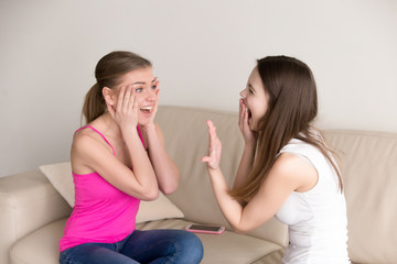 Young happy girl screaming in joy while showing her precious expensive diamond ring to surprised girlfriend. Best friends celebrate one of them getting engaged. Girl received proposal, romantic gift.