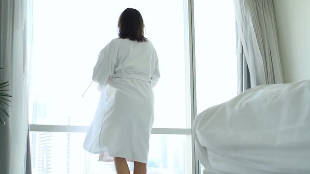 Woman putting on bathrobe by window at home and admire view

