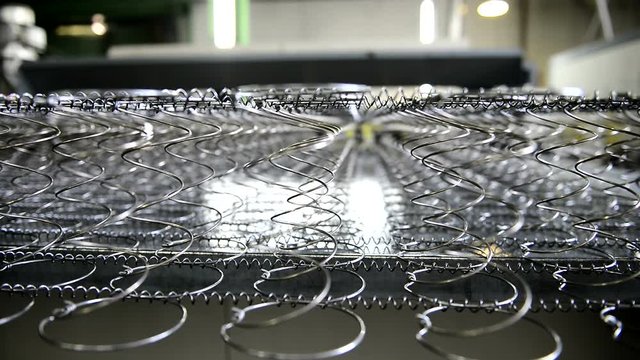 Machine produces an orthopedic mattress with springs. Metal frame moves on table and trembles with powerful work.