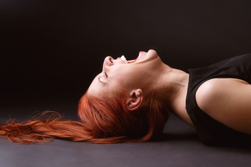Red-haired woman lying ob the floor and hysterically laughing