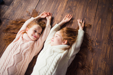 twin sisters in knitted sweaters lying on the floor - obrazy, fototapety, plakaty