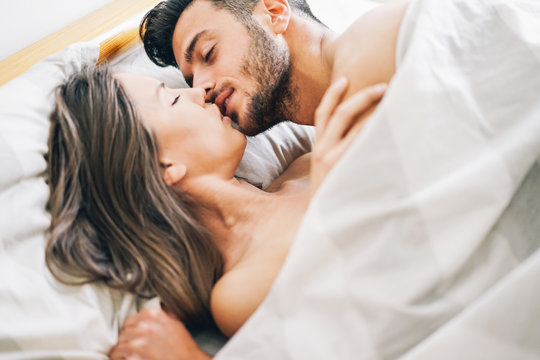 Young couple in love kissing in a bed under white blanket 