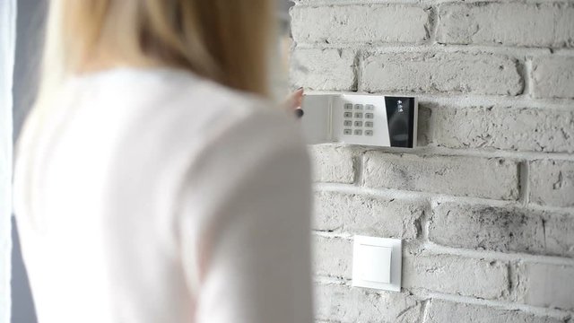 Woman entering pin on home security alarm keypad on the wall