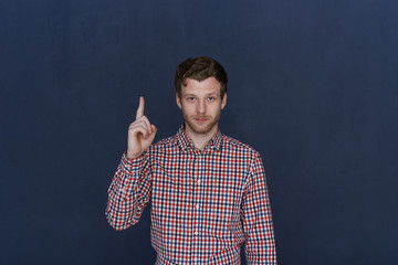 I have an idea. Waist up shot of handsome positive young man with trimmed beard smiling, raising...