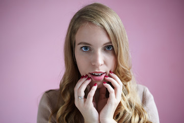 Portrait of charming gorgeous young woman with beautiful curly hair, pink lipstick and manicured nails posing at purple studio wall, looking at camera with lips slightly parted and amazed eyes