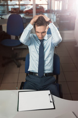 horrified over empty document/ Office employee of the office in a shirt and tie is horrified over an empty document template by white paper on the desk. Holds his hair because of stress and horror