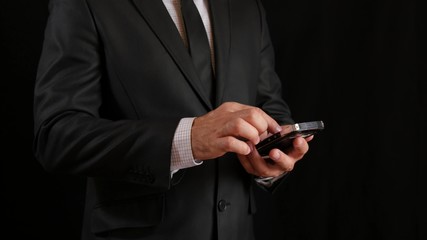 Concept, digital online life and social networks. A businessman in a black business suit with a tie uses his smartphone to view his accounts.