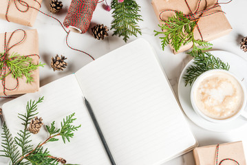 Blank notebook and pencil for wishes, to do list, coffee mug, Christmas gift or present box, decorated with christmas tree branches, pine cones, red berries, on white marble table, copy space top view