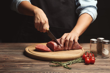 Chef cutting fresh raw meat on wooden board