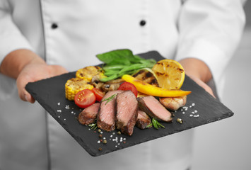 Chef with slate plate with tasty meat, closeup
