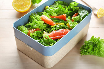 Delicious salad with salmon in lunch box on table