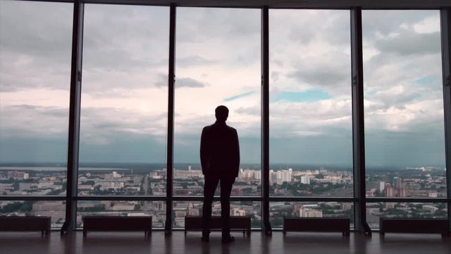 Rear view of businessman in an office with panoramic city view. Businessman admires the city from the panoramic Windows in the city centre