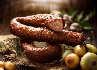 Smoked  sausage on a wooden rustic table with addition of fresh aromatic herbs and spices, natural...