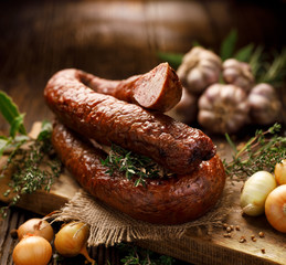 Smoked  sausage on a wooden rustic table with addition of fresh aromatic herbs and spices, natural product from organic farm, produced by traditional methods