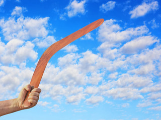 Australian Boomerang in men hand against of cloudy blue sky.