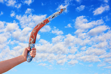 Australian Boomerang in men arm against of cloudy blue sky.
