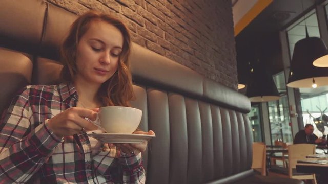 Woman drinking coffee in a cafe, 4K Slow Motion 120 fps. Stabilazed dolly shot. Young beautiful calm woman enjoying a cup of hot coffee in the restaurant. Relaxed morning breakfast in a city. 