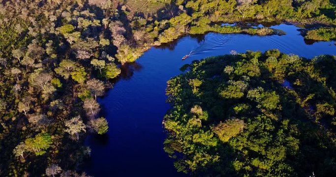 Boat on the river with forest on the edges. Aerial image in the Pantanal Biome. Boat sails on blue water river. Vegetation of riparian forest.  Mato Grosso do Sul state, Central-Western - Brazil.