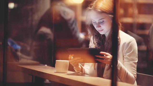 Portrait of Young Woman Using Digital Tablet in Cafe at Night. 4K. Elegant businesswoman drinking coffee, reading news on tablet computer, using app, shopping, communicating in social media. 