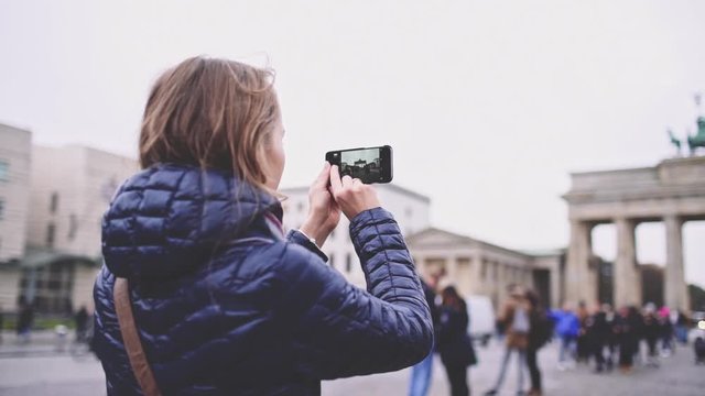 Woman Taking Pictures of Brandenburg Gate in Berlin with SmartPhone. SLOW MOTION. Young woman tourist with cellphone photographing Brandenburger Tor. Travel in Germany.