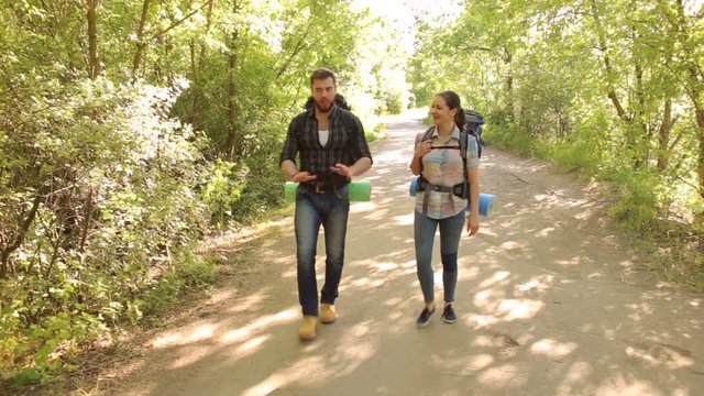Two travelers with large backpacks on their back walk along the road in the forest in the summer. Active rest in summer.