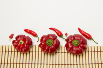 Several ripe sweet and hot peppers on a straw napkin on a white background