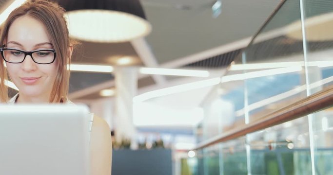Portrait of Businesswoman Working on Laptop at Co-Working Space. 4K SLOW MOTION, DCi. Young business woman, wearing glasses, using portable computer in the modern office building. Technology in Life