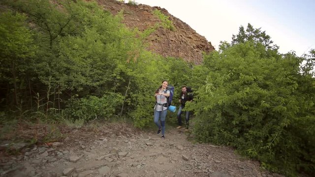 Two tourists walk on a rocky trail in the mountains with large backpacks.