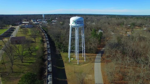 Drone flight by a water tower in Harlem Georgia. Clear blue sky with a train below.