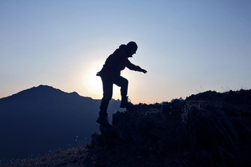 silhouette of a man who climbs the mountain on a background of dawn.